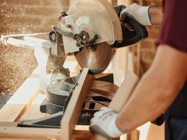 Person using a mitre saw to cut a length of timber, with wood dust visible around the blade, illustrating professional joinery, woodworking and DIY installation projects.