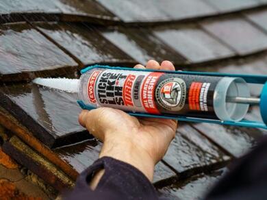 Evostik Sticks Like Turbo clear adhesive cartridge being applied to a wet roof tile during an outdoor repair, demonstrating high-strength grab adhesive performance in damp weather conditions.