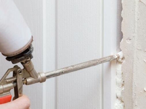 Close-up of expanding foam being injected into a gap between a wall and door frame with a foam gun, creating an insulated and airtight seal.