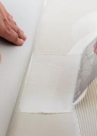 Close-up of a trowel applying and smoothing flooring adhesive on a textured subfloor, demonstrating floor preparation for adhesive installation.