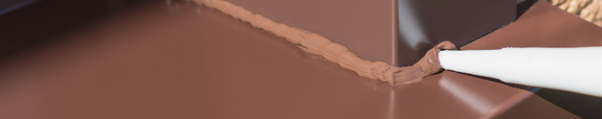 A brown metal corner being sealed with a bead of brown sealant applied with a sealant gun