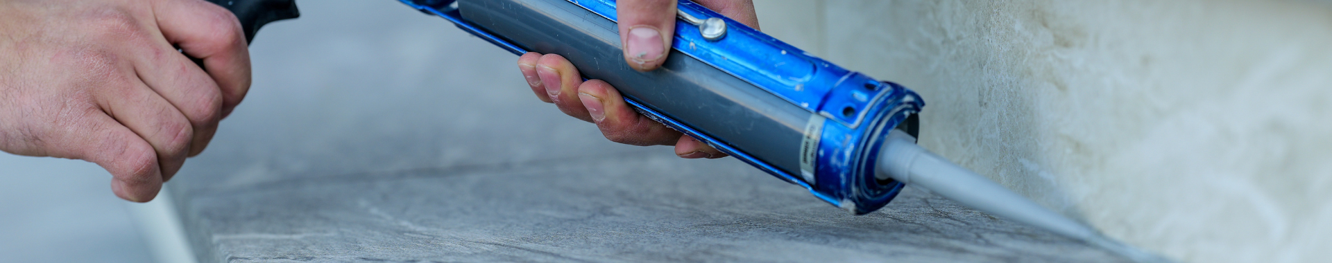 A man using a blue caulking gun to seal a gap on stone stairs