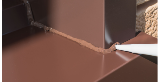 A brown metal corner being sealed with a bead of brown sealant applied with a sealant gun