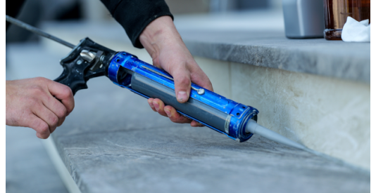 A man using a blue caulking gun to seal a gap on stone stairs